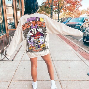 May include: A cream colored sweatshirt with a graphic print of Minnie Mouse dressed as a vampire. The graphic says "Minnie's Halloween" and "Trick or Treat" with a candy corn design.