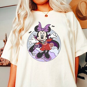 May include: A white t-shirt with a cartoon image of a vampire Minnie Mouse wearing a purple cape and holding a bat. The image is surrounded by a purple and blue circle with white clouds and stars. The text "Do Not Copy" appears multiple times around the image.
