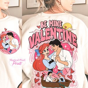 May include: White sweatshirt with a pink graphic design featuring Ariel and Prince Eric from The Little Mermaid. The graphic says "Be Mine Valentine" with hearts and stars.
