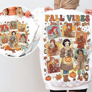May include: White sweatshirt featuring a colorful graphic of cartoon princesses in fall attire. The design includes pumpkins, leaves, and the text "FALL VIBES just a fall girl". The princesses are depicted in polaroid-style frames.