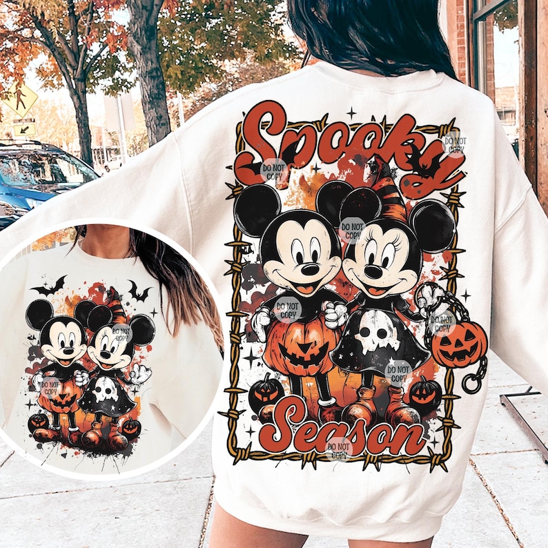 May include: Cream-colored sweatshirt featuring a Halloween-themed graphic. The design includes Mickey and Minnie Mouse dressed in Halloween costumes, surrounded by pumpkins and the words "Spooky Season" in orange and red. The image is framed by a barbed wire design.