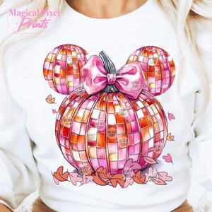 K&ouml;nnte beinhalten: Ein wei&szlig;er Pullover mit einem pinkfarbenen und orangenen K&uuml;rbisdesign. Der K&uuml;rbis ist in Form von Mickey-Maus-Ohren geformt und hat eine rosafarbene Schleife. Der K&uuml;rbis besteht aus einem Mosaik aus Quadraten und hat einen Aquarelleffekt. Um den K&uuml;rbis herum befinden sich kleine rosa und orangefarbene Bl&auml;tter.