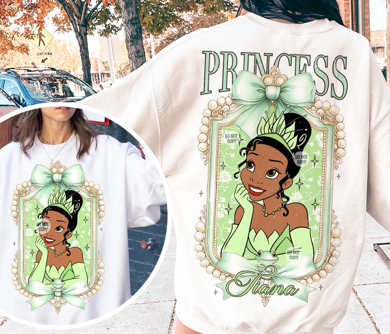 May include: White sweatshirt with a green and gold princess design featuring a cartoon image of Tiana from Disney's The Princess and the Frog. The text "Princess" is printed above the design and "Tiana" is printed below the design.