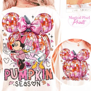 K&ouml;nnte beinhalten: Ein wei&szlig;es T-Shirt mit einem pinkfarbenen und orangenen K&uuml;rbisdesign. Der K&uuml;rbis besteht aus einer Discokugel und hat eine rosa Schleife oben drauf. Mickey Mouse und Daisy Duck stehen vor dem K&uuml;rbis. Der Text "Pumpkin Season" steht unter dem K&uuml;rbis.