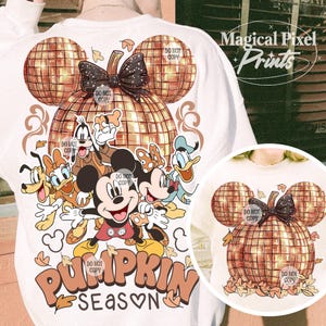 K&ouml;nnte beinhalten: Ein wei&szlig;es Sweatshirt mit einem goldenen Glitzerk&uuml;rbis-Design mit Mickey Mouse und seinen Freunden. Der K&uuml;rbis ist in Form von Mickey Mouse-Ohren und hat eine schwarze Schleife. Der Text "Pumpkin Season" ist in orangefarbenen und braunen Buchstaben unter dem K&uuml;rbis geschrieben.