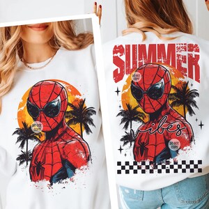 May include: White sweatshirt with a red and blue Spiderman graphic wearing sunglasses and a sunset background. The text "Summer Vibes" is printed in red on the back of the sweatshirt.