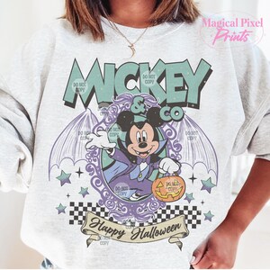 Puede incluir: Una sudadera blanca con un gr&aacute;fico de estilo vintage de Mickey Mouse vestido de vampiro sosteniendo una calabaza de Halloween. El gr&aacute;fico incluye el texto "Mickey & Co" y "Happy Halloween".