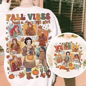 May include: White long-sleeve sweatshirt with the text "FALL VIBES just a tall girl." The design features illustrations of cartoon characters in fall attire, surrounded by autumn leaves and pumpkins. The design is repeated on the smaller image.