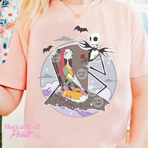 May include: A pink t-shirt with a graphic print of Jack Skellington and Sally from the Nightmare Before Christmas movie. The characters are standing in front of a tombstone with a rose.