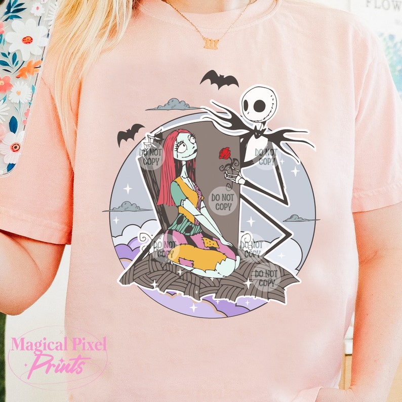 May include: A pink t-shirt with a graphic print of Jack Skellington and Sally from the Nightmare Before Christmas movie. The characters are standing in front of a tombstone with a rose.