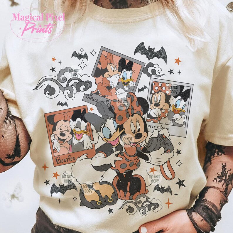 Op de afbeelding: Een wit T-shirt met een kleurrijke grafische print met Mickey Mouse en Minnie Mouse-figuren. Het ontwerp bevat afbeeldingen van de personages in verschillende poses, samen met de tekst "Girls Rule" en "Best Friends".