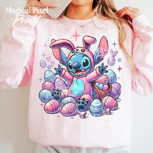 May include: A pink sweatshirt with a blue and pink cartoon character wearing a bunny costume. The character is surrounded by pastel colored Easter eggs.