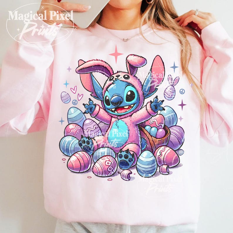 May include: A pink sweatshirt with a blue and pink cartoon character wearing a bunny costume. The character is surrounded by pastel colored Easter eggs.