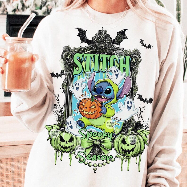 May include: White sweatshirt featuring a Halloween-themed graphic. The design includes Stitch dressed in a green hooded costume holding a pumpkin, surrounded by ghosts. The words "Stitch" and "Spooky Season" are also displayed.