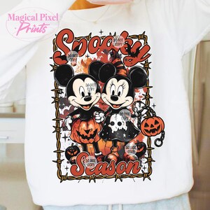 May include: White sweatshirt featuring Mickey and Minnie Mouse in Halloween costumes. The design includes the words "Spooky Season" and jack-o'-lanterns. The image is framed with a barbed wire design.