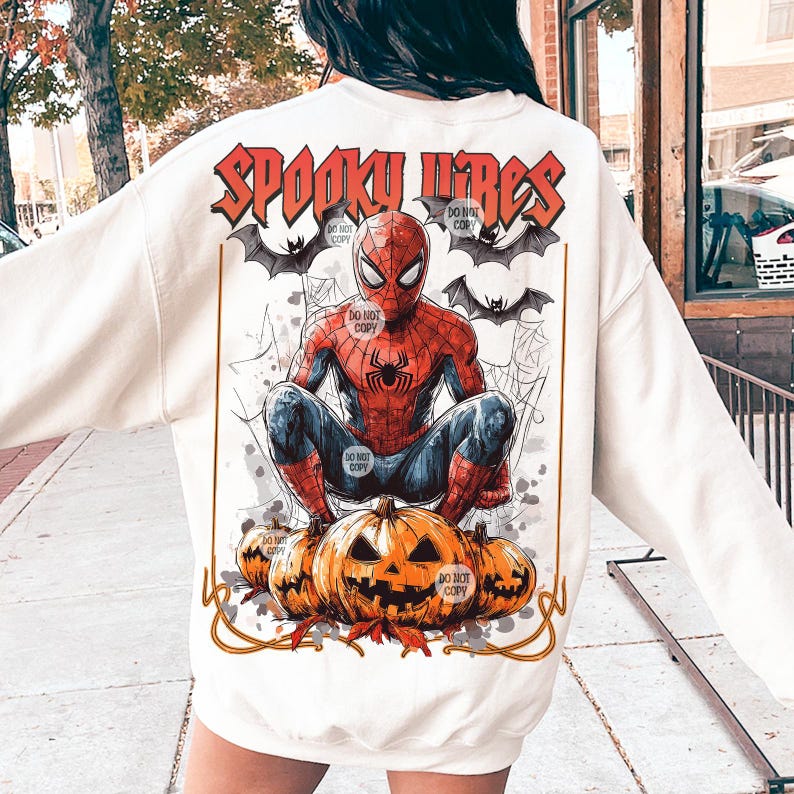 K&ouml;nnte beinhalten: Cremefarbenes Sweatshirt mit einer Grafik von Spider-Man auf K&uuml;rbissen. Das Design umfasst Flederm&auml;use, Spinnweben und den Text "SPOOKY VIBES" in Orange. Ein Kleidungsst&uuml;ck zum Thema Halloween.