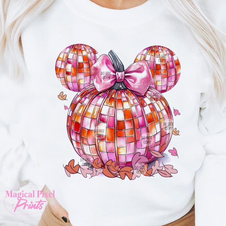 K&ouml;nnte beinhalten: Ein wei&szlig;es T-Shirt mit einem Design aus einem rosa und orangefarbenen K&uuml;rbis. Der K&uuml;rbis ist in Form von Mickey-Maus-Ohren und hat eine rosa Schleife. Das Design ist von kleinen orangefarbenen Bl&auml;ttern umgeben.