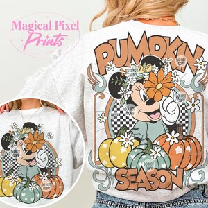 May include: A white sweatshirt with a graphic print of a cartoon mouse wearing a flower crown and holding a pumpkin. The graphic also includes the text "Pumpkin Season" and a checkered pattern.