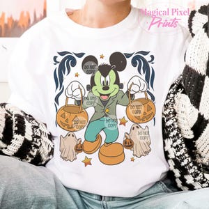 May include: A white t-shirt with a green and black Mickey Mouse dressed as a monster holding two orange jack-o'-lantern buckets. The shirt has the text "DO NOT COPY" repeated multiple times.