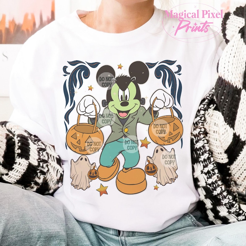 May include: A white t-shirt with a green and black Mickey Mouse dressed as a monster holding two orange jack-o'-lantern buckets. The shirt has the text "DO NOT COPY" repeated multiple times.