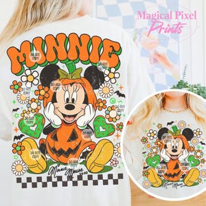 May include: Cream-colored t-shirt featuring a Halloween-themed Minnie Mouse design. The graphic shows Minnie in a pumpkin costume, surrounded by flowers, hearts, and bats. The word "MINNIE" is arched across the top. Text includes "Minnie Mouse" and "xoxo".