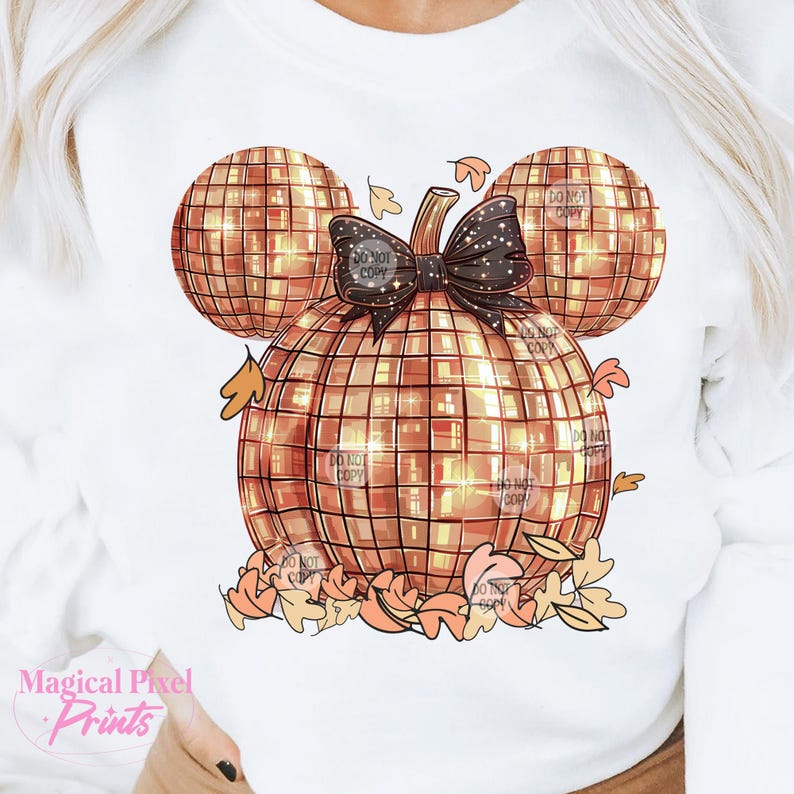 K&ouml;nnte beinhalten: Ein wei&szlig;es Sweatshirt mit einem goldenen Glitzerk&uuml;rbis-Design in Form von Mickey Mouse-Ohren. Der K&uuml;rbis hat eine schwarze Schleife und ist von orangefarbenen und braunen Bl&auml;ttern umgeben.