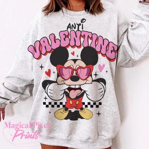 Pu&ograve; includere: Una felpa grigia con una grafica rosa e bianca di Topolino che indossa occhiali a forma di cuore e il testo "Anti Valentine".