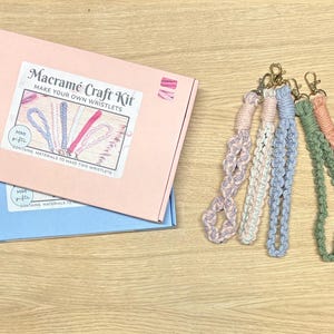 May include: A pink and blue box with the text "Macrame Craft Kit Make Your Own Wristlets" and a picture of macrame wristlets. The box contains materials to make two wristlets.