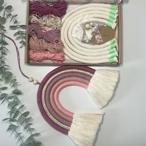May include: A DIY rainbow wall hanging kit with pink, purple, and gold yarn, white rope, and wooden beads. The kit includes instructions for creating a rainbow with tassels.