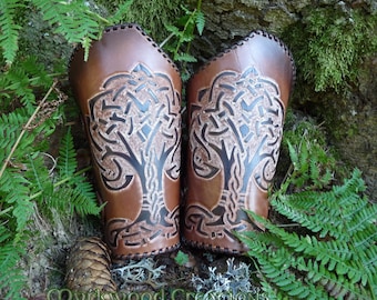 May include: A pair of brown leather arm guards with a Celtic knotwork tree design. The guards are decorated with a light brown and dark brown pattern.