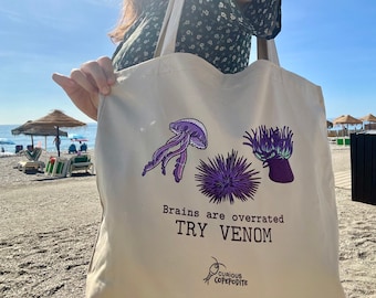 May include: A white tote bag with a purple jellyfish, sea anemone, and sea urchin design. The bag has the text "Brains are overrated TRY VENOM" and a small logo that says "Curious Copepodite".