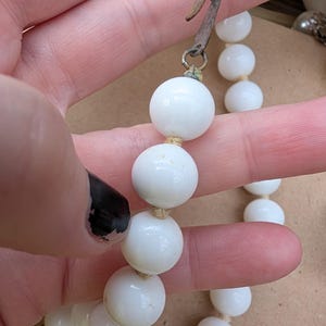 May include: A vintage white beaded necklace with a metal clasp. The necklace features large, round beads strung together. The clasp is a tarnished metal color. The beads are a bright white color.