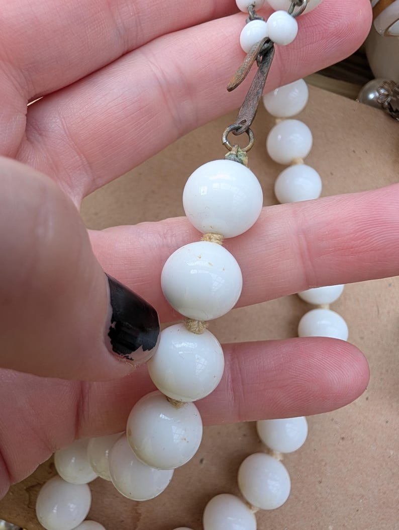 May include: A vintage white beaded necklace with a metal clasp. The necklace features large, round beads strung together. The clasp is a tarnished metal color. The beads are a bright white color.