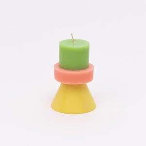 Könnte beinhalten: Eine grüne Kerze sitzt auf einem rosa und gelben Kerzenhalter. Der Halter ist kegelförmig mit einem Ring oben.