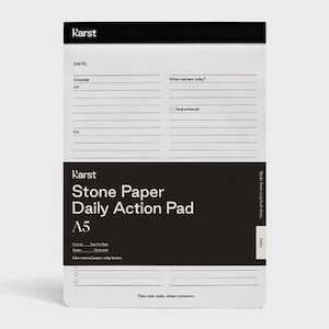 May include: A white Karst Stone Paper Daily Action Pad A5. The pad has a black band at the top and a black band at the bottom with the product name. It includes sections for scheduling, goals, and notes. The text "Take note today, shape tomorrow" is at the bottom.