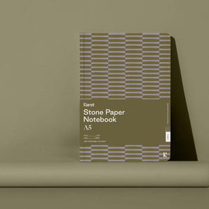 Op de afbeelding: Een rechthoekig A5-notitieboek van steenpapier met een geometrisch patroon in olijfgroen en lavendel. Het notitieboek is van het merk "Karst Stone Paper Notebook" en wordt gepresenteerd op een neutrale achtergrond.