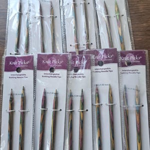 May include: A collection of Knit Picks interchangeable knitting needle tips in various sizes, packaged in clear plastic. The wooden needles have a colorful, striped pattern. The packaging includes the Knit Picks logo and needle size.