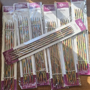 May include: Multiple sets of Knit Picks double-pointed knitting needles. The needles are packaged in clear plastic with purple and white labels. The needles have a colorful, speckled design in shades of brown, green, and yellow.