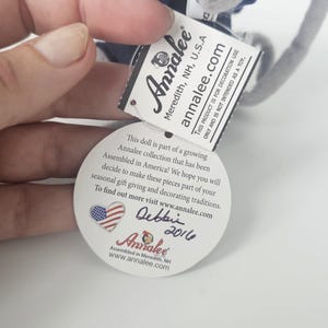 Puede incluir: Una peque&ntilde;a mu&ntilde;eca Annalee con uniforme azul con una etiqueta que dice "Annalee Meredith, NH, U.S.A.". La etiqueta tambi&eacute;n incluye el texto "Este producto es para uso decorativo &uacute;nicamente y no est&aacute; destinado a ser un juguete."