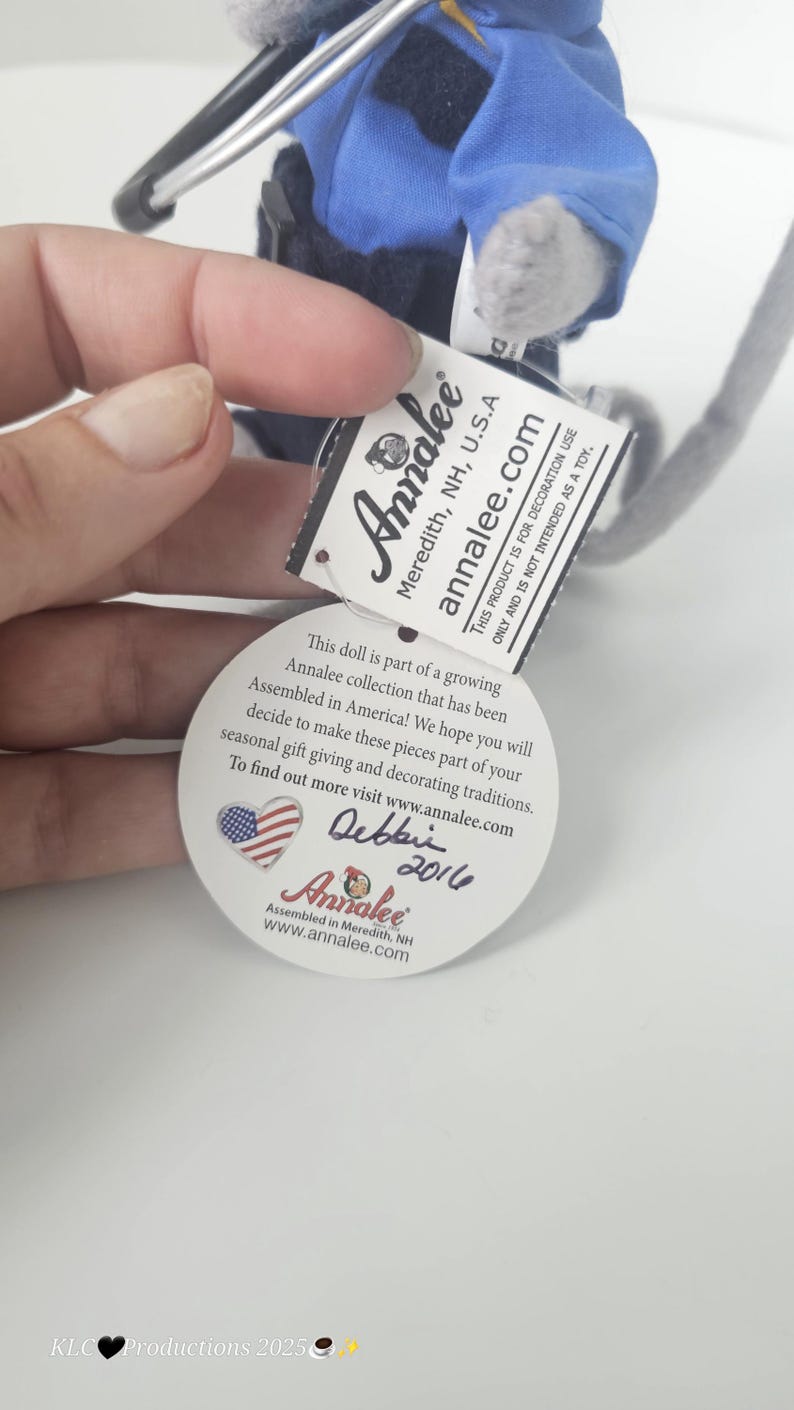 Puede incluir: Una peque&ntilde;a mu&ntilde;eca Annalee con uniforme azul con una etiqueta que dice "Annalee Meredith, NH, U.S.A.". La etiqueta tambi&eacute;n incluye el texto "Este producto es para uso decorativo &uacute;nicamente y no est&aacute; destinado a ser un juguete."