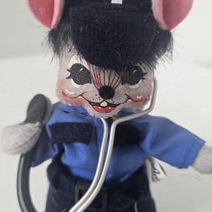 Puede incluir: Un peluche de rat&oacute;n vestido de param&eacute;dico, con uniforme azul y gorro azul marino con un s&iacute;mbolo m&eacute;dico blanco. El rat&oacute;n tiene orejas rosas y sostiene un estetoscopio. Un art&iacute;culo de novedad.
