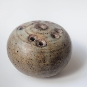 May include: A spherical, ceramic object with a speckled, mottled surface in shades of brown and gray. The object has several circular holes on its top surface. The overall design suggests a decorative or functional item, possibly for home decor.