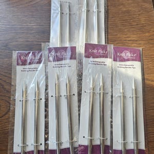 May include: Several packages of Knit Picks Options interchangeable knitting needle tips. The packages are clear with a purple and white label. The text on the label reads "Interchangeable Knitting Needle Tips" and "Traveling the world to bring you affordable knitting."