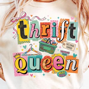 Puede incluir: Camiseta color crema con un diseño gráfico colorido. El diseño presenta las palabras "thrift queen" en una fuente lúdica, junto con una cesta de la compra, una percha y las palabras "second hand" y "vintage find". El diseño está acentuado con corazones y estrellas.