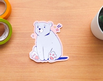 May include: A sticker featuring a cartoon illustration of a light blue polar bear with pink paws sitting down. The bear has a surprised expression and a pink star is behind it.