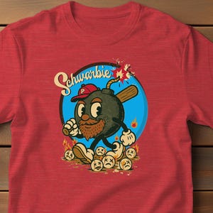 May include: Red t-shirt featuring a cartoon bomb character with a baseball bat, wearing a baseball cap. The character is surrounded by flames and sad-faced baseballs. The word "Schwarbie" is written above the character in a blue circle.