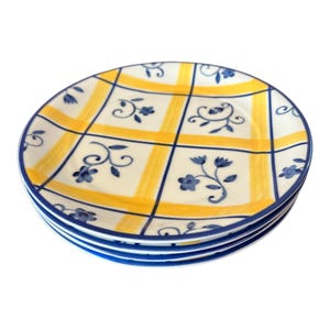May include: A stack of four ceramic plates with a yellow and white checkered pattern. Each plate has blue floral accents and a blue border. The plates are stacked on top of each other.