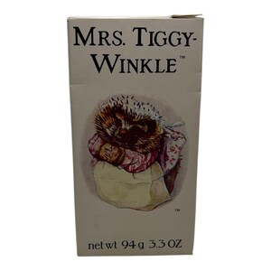 Puede incluir: Caja con el texto "MRS. TIGGY-WINKLE" y una ilustración de un erizo con gorro y manta. También incluye el texto "net wt 94 g 3.3 OZ". La ilustración está en tonos suaves de acuarela.