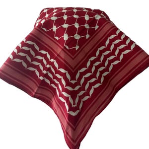 May include: A red and white patterned bandana. The bandana features a repeating white leaf-like design and a white dotted pattern. The edges have a striped border in shades of red. The bandana is folded in a square shape.