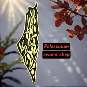 May include: A gold-colored outline of the country of Palestine with an olive branch design inside. The text "Palestinian owned shop" is below the outline.